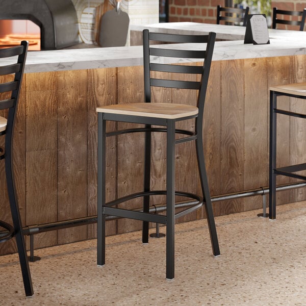 A black metal ladder back bar stool with a driftwood-colored wooden seat.
