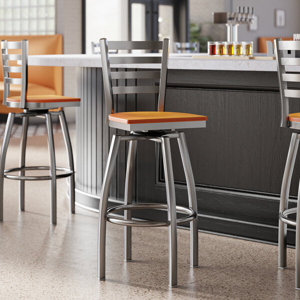 Lancaster Table & Seating Clear Coat Finish Ladder Back Swivel Bar Stools with Cherry Wood Seats at a bar counter.
