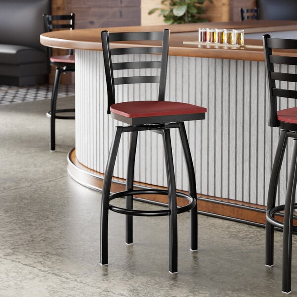 A black metal ladder back swivel bar stool with a mahogany wood seat.