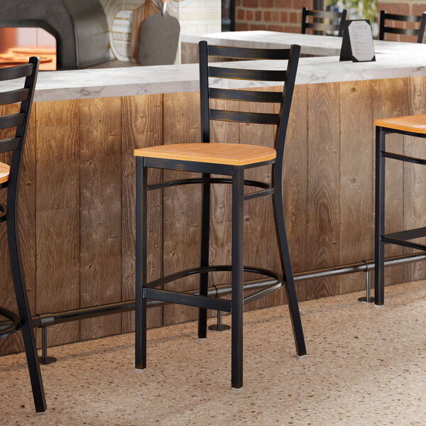 A bar stool with a distressed copper finish ladder back and a natural wood seat.