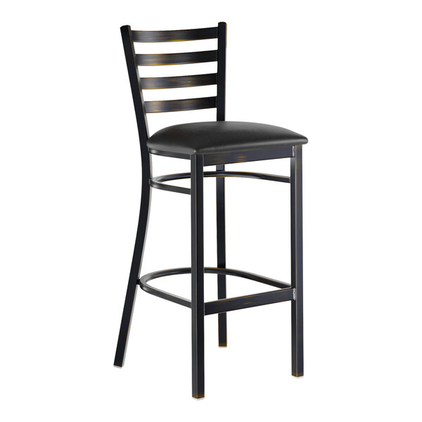 A metal ladder back bar stool with a distressed copper finish and a black vinyl padded seat.