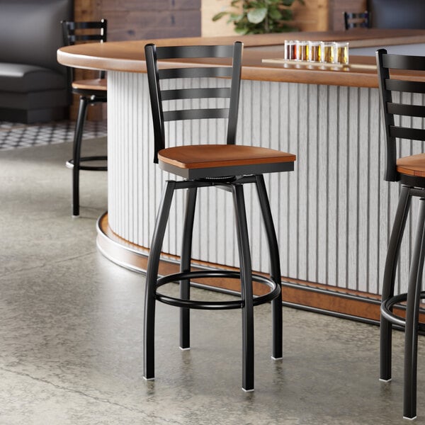 A black metal ladder back swivel bar stool with an antique walnut wood seat.