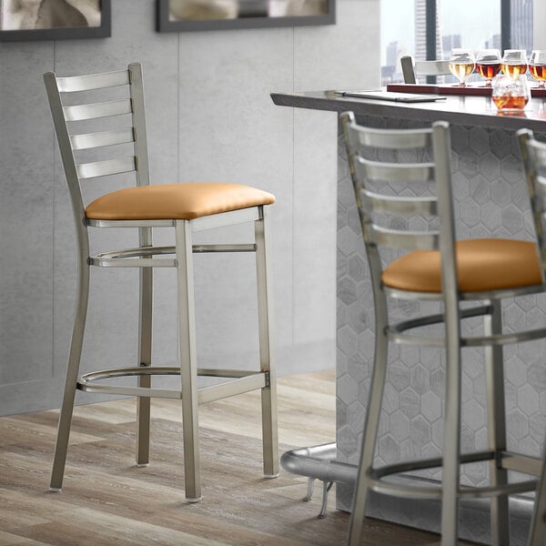 A Lancaster Table & Seating ladder back bar stool with a light brown vinyl cushion on a bar counter.