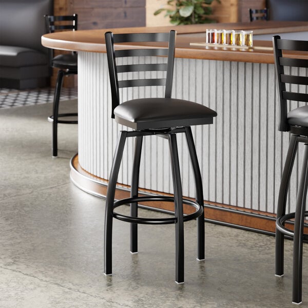 A black finish ladder back swivel bar stool with a 2 1/2 inch black vinyl padded seat.