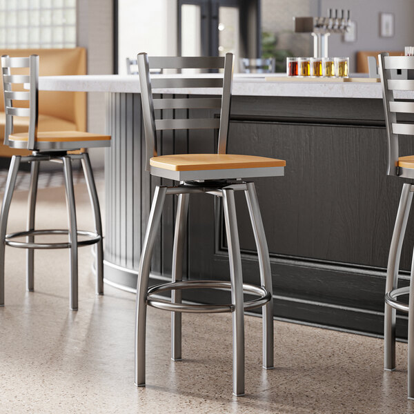 A group of Lancaster Table & Seating ladder back swivel bar stools with natural wood seats next to a counter.