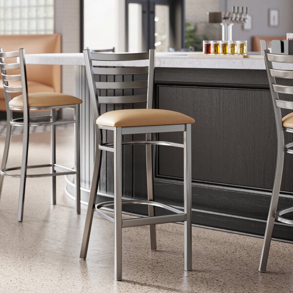 A group of Lancaster Table & Seating clear coat finish ladder back bar stools with light brown vinyl padded seats at a counter.