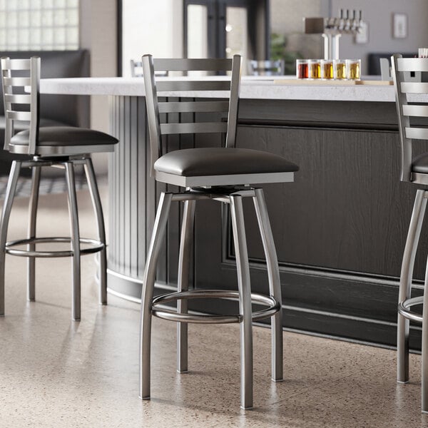 A group of Lancaster Table & Seating ladder back bar stools with black vinyl padded seats next to a counter.