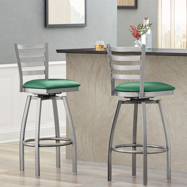 Two Lancaster Table & Seating metal bar stools with green vinyl padded seats.