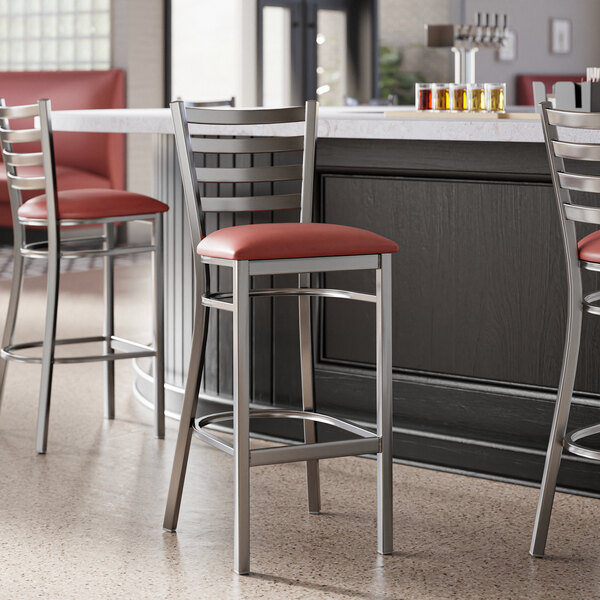 A metal bar stool with a ladder back design and a burgundy vinyl padded seat.