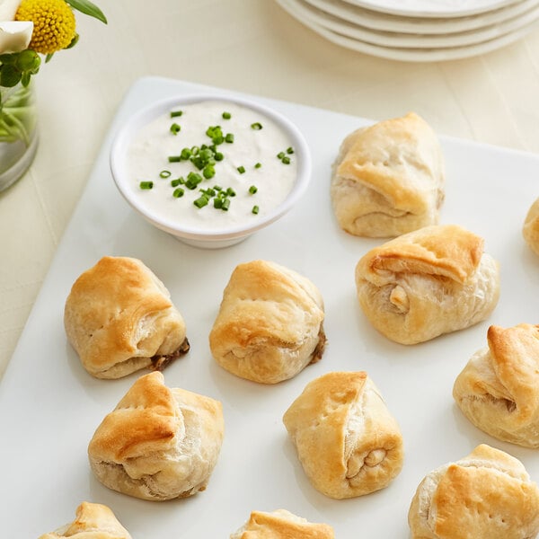 A plate of Les Chateaux de France Beef Wellington En Croute with white sauce and green onions for dipping.