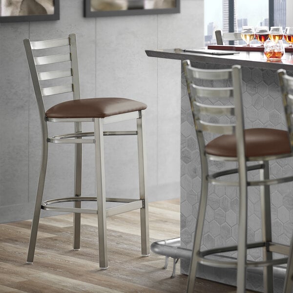 A Lancaster Table & Seating ladder back bar stool with a dark brown cushioned seat.