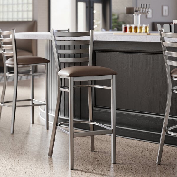 A Lancaster Table & Seating ladder back bar stool with dark brown vinyl padded seat.