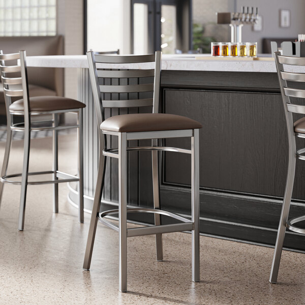 A metal bar stool with a ladder back design and a dark brown vinyl padded seat.