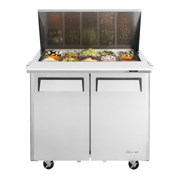 A Turbo Air refrigerated sandwich prep table with food trays on top.