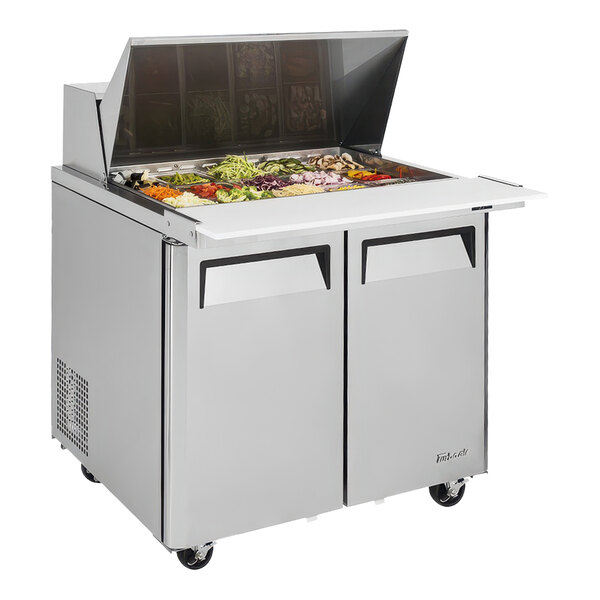A Turbo Air sandwich prep table with a stainless steel top on wheels.