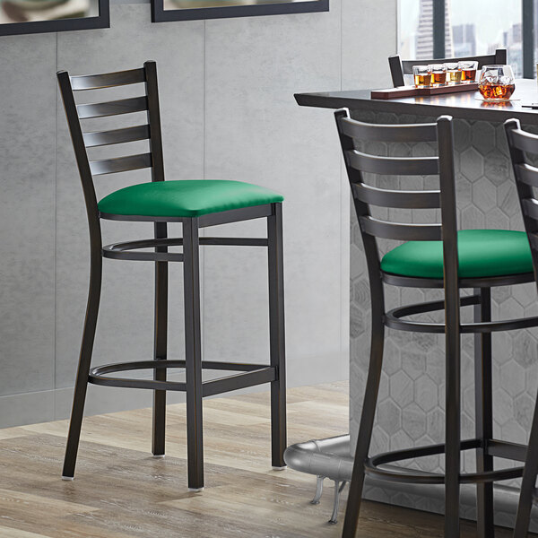A Lancaster Table & Seating ladder back bar stool with a green vinyl padded seat.