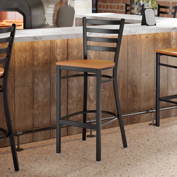 A black ladder back bar stool with a cherry wood seat positioned at a counter.