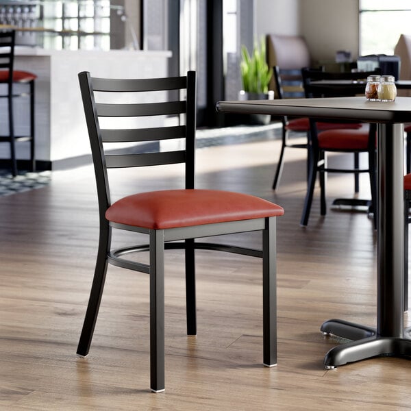 A black ladder back chair with a burgundy vinyl padded seat.