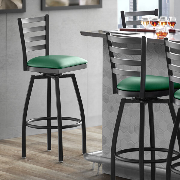 A Lancaster Table & Seating black ladder back swivel bar stool with a green cushion.