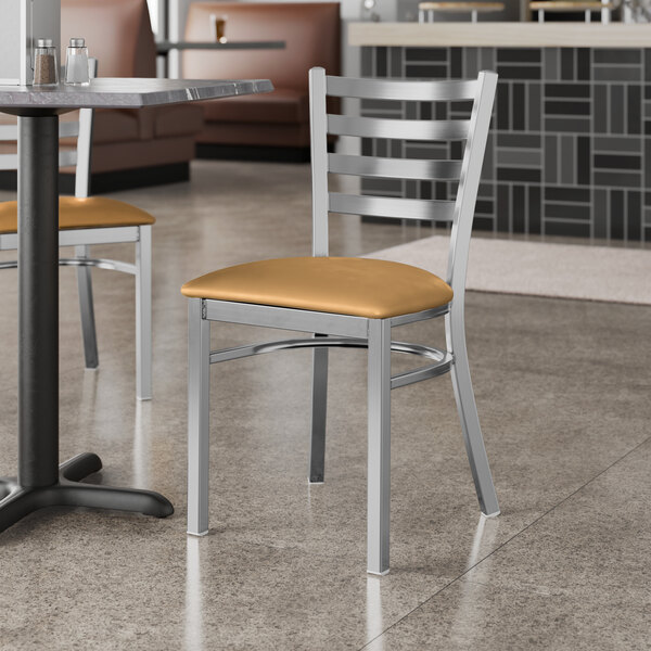 A Lancaster Table & Seating ladder back chair with a light brown vinyl padded seat at a table in a restaurant.