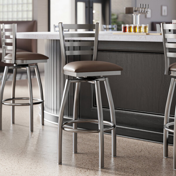 A group of Lancaster Table & Seating swivel bar stools with dark brown vinyl padded seats next to a counter.