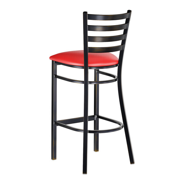 A metal bar stool with a ladder back design and a red vinyl padded seat.