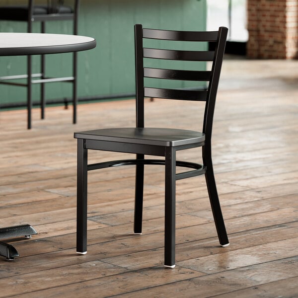 A Lancaster Table & Seating black metal ladder back chair with black wood seat on a wood floor.