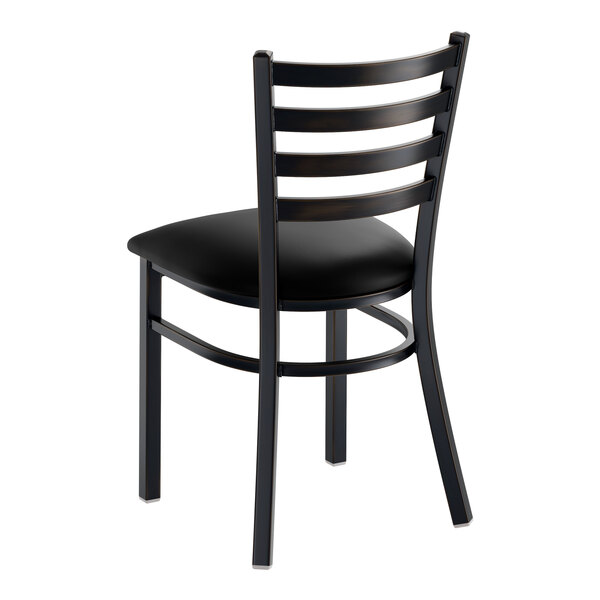 A black ladder back chair with a padded vinyl seat and a distressed copper finish.
