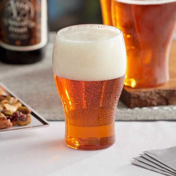 A Visions clear plastic beer glass full of beer with foam on top on a table in a bar.