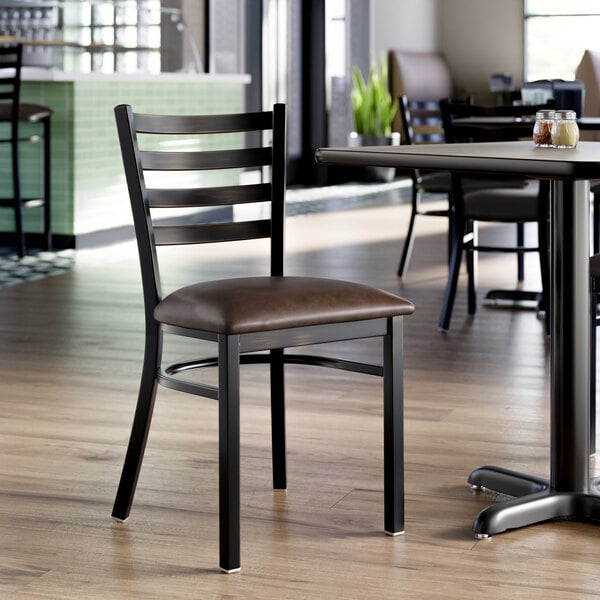 A metal ladder back chair with a dark brown vinyl padded seat and a distressed copper finish, placed in a restaurant setting.