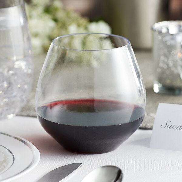 A Visions clear plastic stemless wine glass filled with red wine on a table.