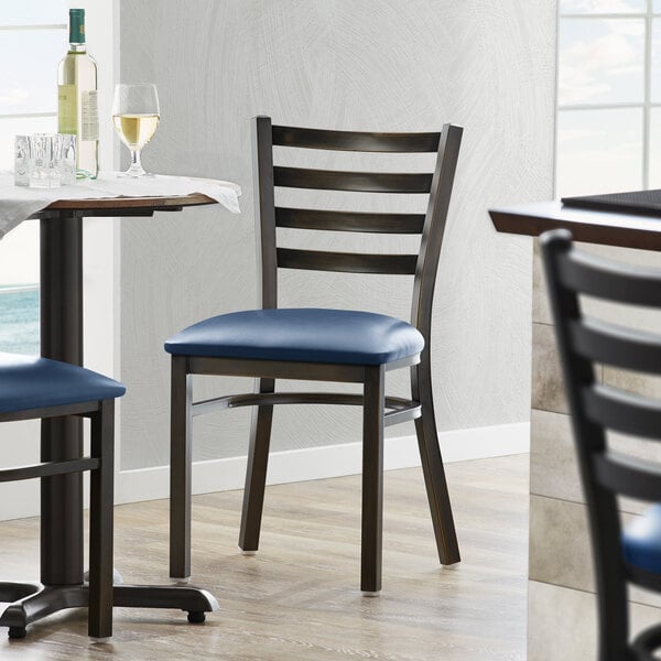 A Lancaster Table & Seating distressed copper ladder back chair with a navy vinyl padded seat.