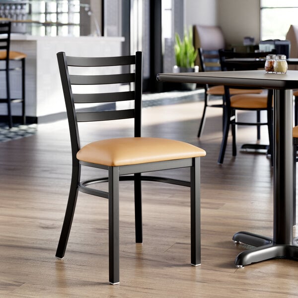 A black ladder back chair with a light brown vinyl padded seat.