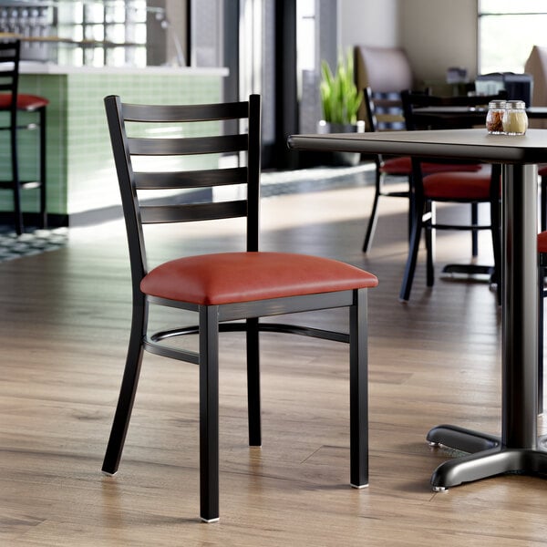 A metal ladder back chair with a burgundy vinyl padded seat and a distressed copper finish, placed in a restaurant setting.