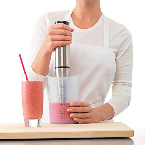 A woman using an iSi translucent silicone measuring cup to make a smoothie.