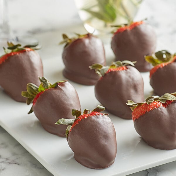 A white plate with chocolate covered strawberries and leaves.