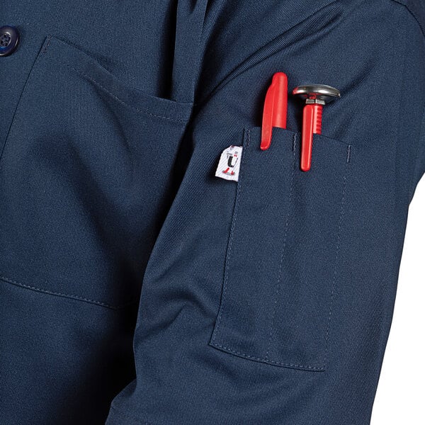 A person wearing a blue Uncommon Chef short sleeve chef coat with tools in the pocket.