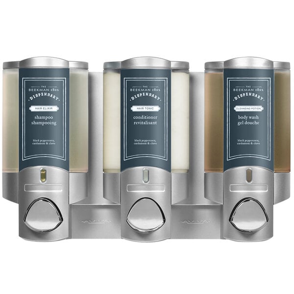 A wall-mounted silver Dispenser Amenities Aviva 3-chamber soap dispenser with Beekman labels.