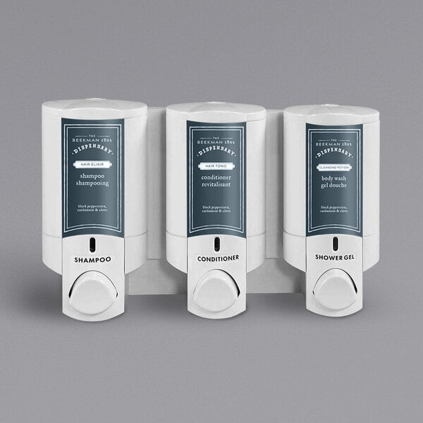 Three white Dispenser Amenities Aviva wall mounted shower dispensers with Beekman labels.