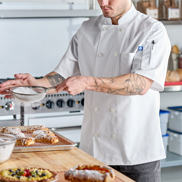 A unisex white short sleeve chef coat in size 4XL being worn by a person in a kitchen.