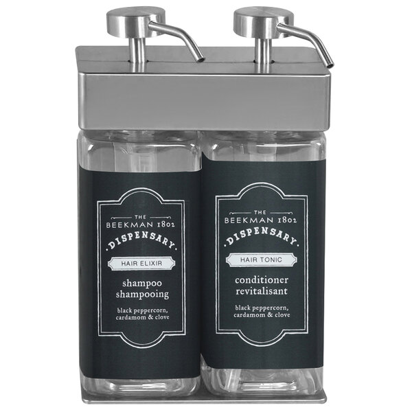 A black wall mounted dispenser with two rectangular bottles of shampoo and conditioner with white Beekman labels.