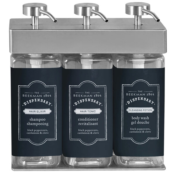 A black wall-mounted dispenser with three rectangular bottles with black and white Beekman labels.