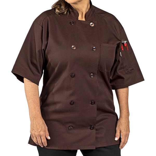 A woman wearing a brown Uncommon Chef short sleeve chef coat with a customizable name tag.