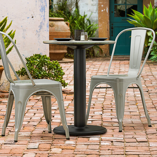A black Lancaster Table & Seating outdoor table base with chairs on a brick patio.