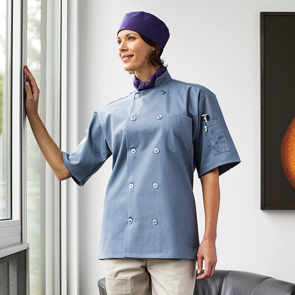 A woman wearing a blue Uncommon Chef short sleeve chef coat with steel buttons.