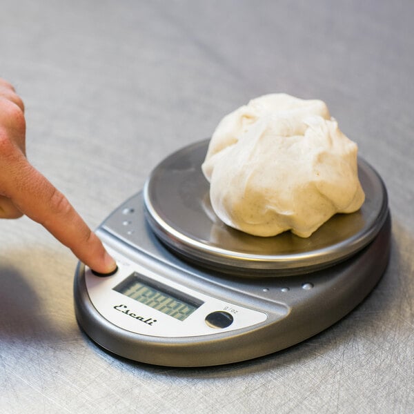 A finger pressing a button on a San Jamar digital kitchen scale.