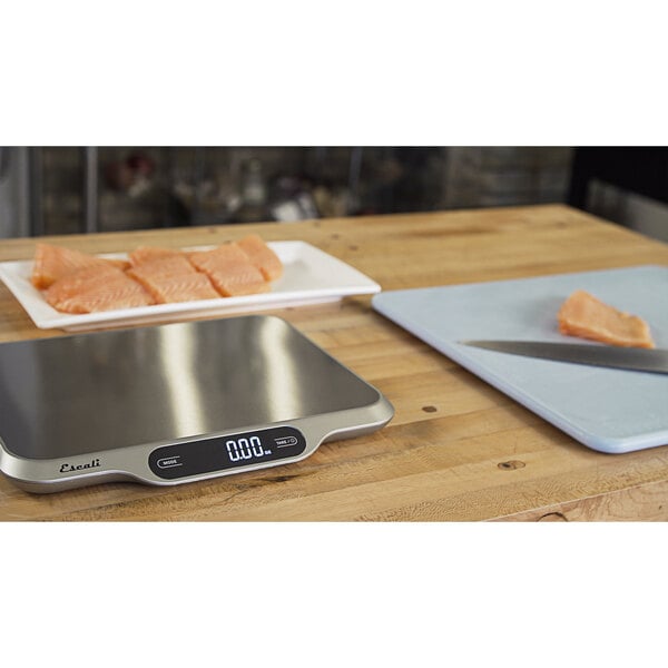 A San Jamar digital kitchen scale on a wood surface with a plate of salmon and a knife.