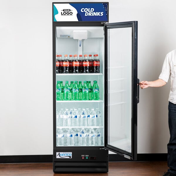 A man opening the swing glass door of a Avantco merchandiser refrigerator full of soda bottles.