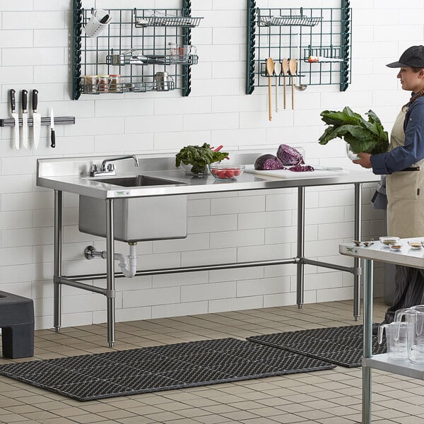 A man standing in a school kitchen using a Regency cross brace on a work table to hold a bowl of vegetables.