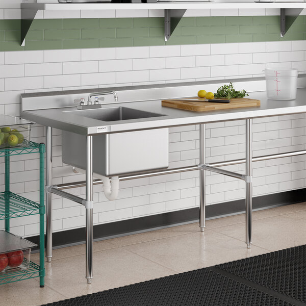 A stainless steel work table with an integrated sink, cross brace supports, and a cutting board with vegetables on top.